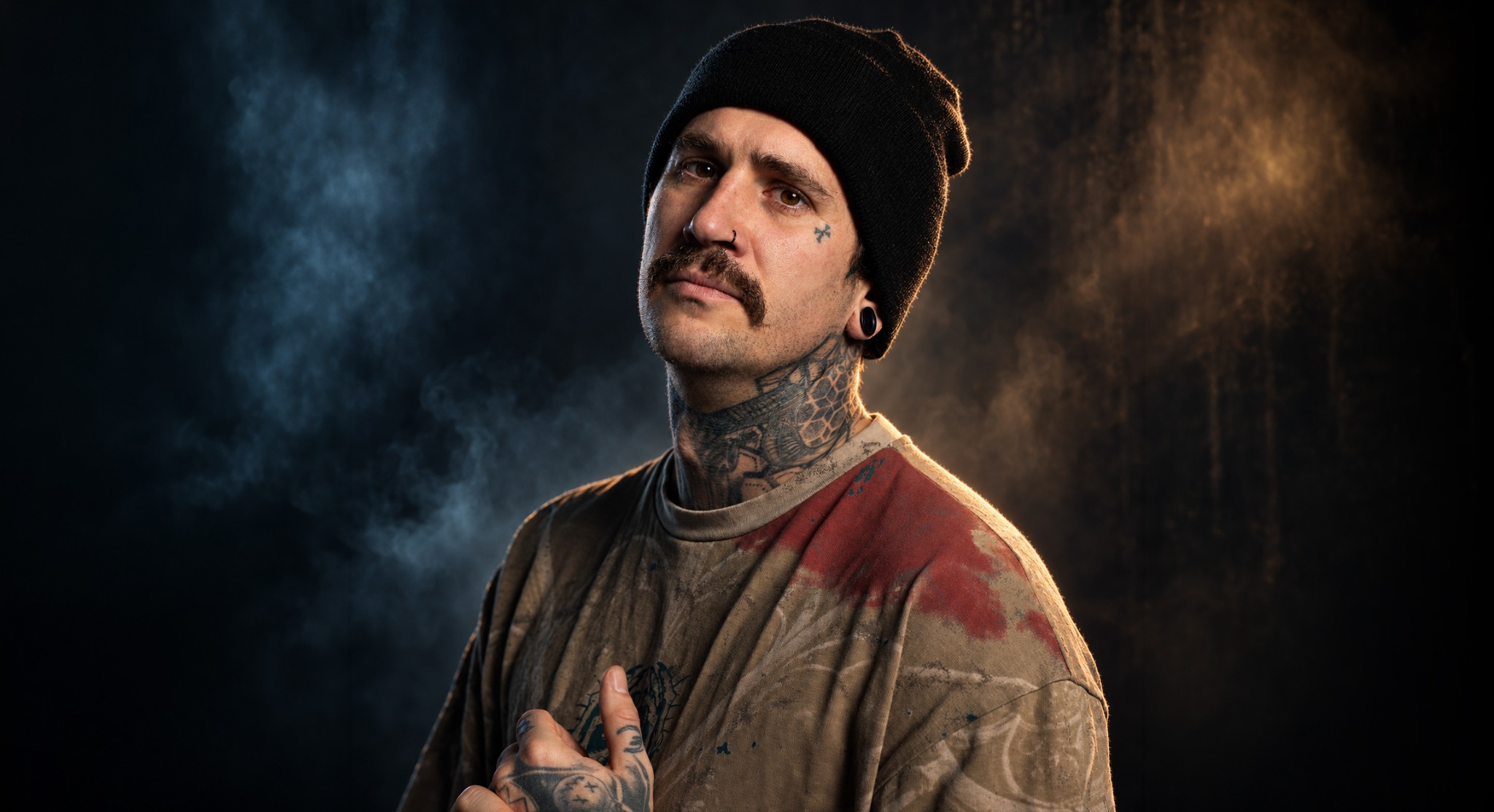 Andreas Ullmann wearing a beanie, with tattoos, against a dark, smoky background